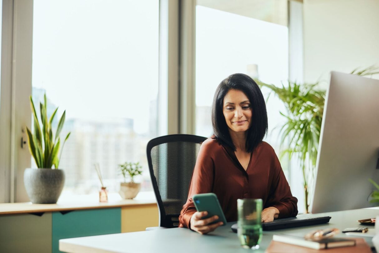 A woman views her mobile phone while working in a modern office.