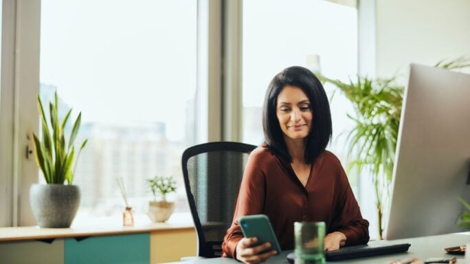 A woman views her mobile phone while working in a modern office.