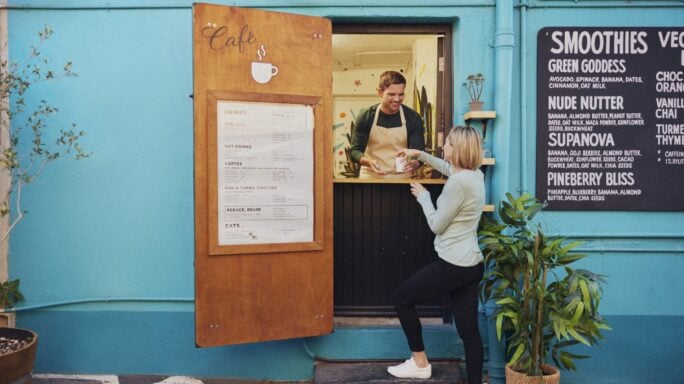 A woman is served a beverage at a cafe serving window.