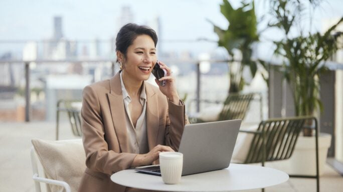 Une femme est assise à une table avec un café et son ordinateur. Elle téléphone