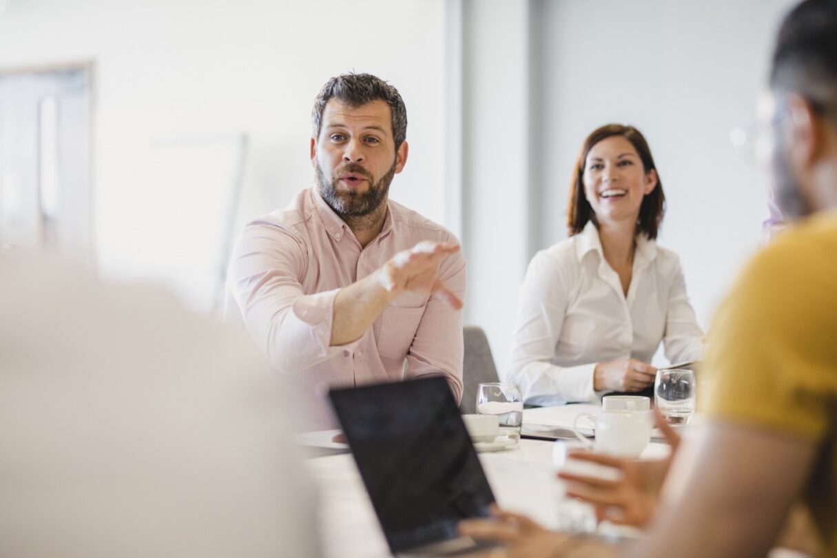 Homem a intervir numa reunião de equipa, sentado à mesa.