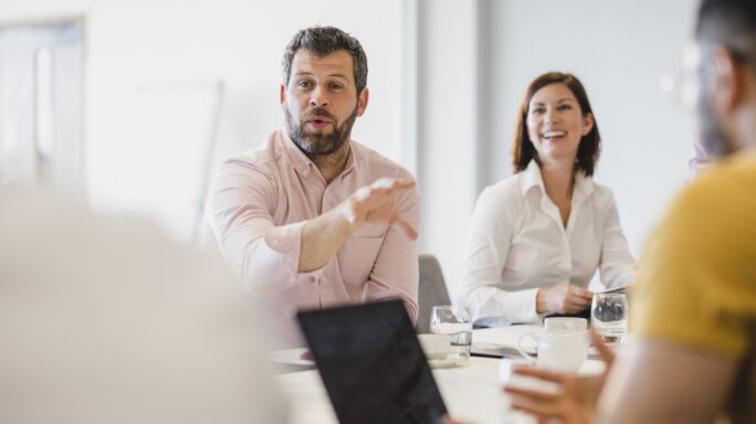 Homem a intervir numa reunião de equipa, sentado à mesa.