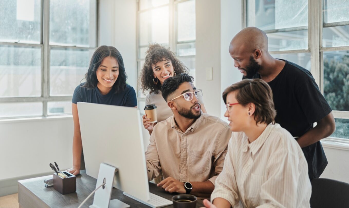 Um grupo de colegas a olhar para um computador, colaborando e discutindo ideias.